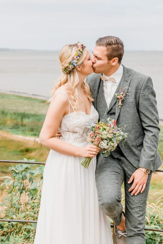 Braut und Bräutigam küssen sich in den Dünen auf der Insel Sylt. Hochzeitsfotografin für Hochzeitsreportage auf Sylt buchen.