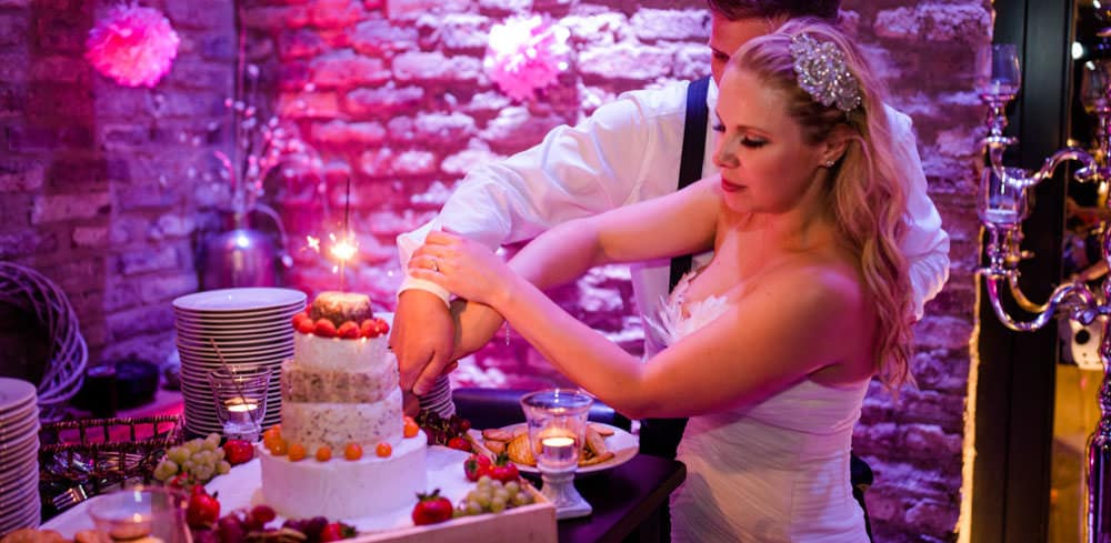 die Hochzeitstorte wird angeschnitten - es ist aber eine Käsetorte aus echtem Käse - natürliche Hochzeitsfotografie voller Liebe